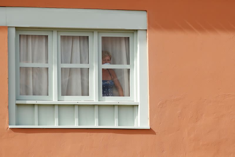 A guest, wearing a protective face mask, looks out from a window at H10 Costa Adeje Palace, which is on lockdown after cases of coronavirus have been detected there in Adeje