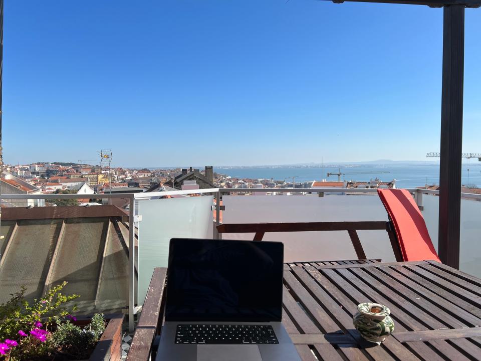 A laptop on a table with an impressive view of a sea and buildings.