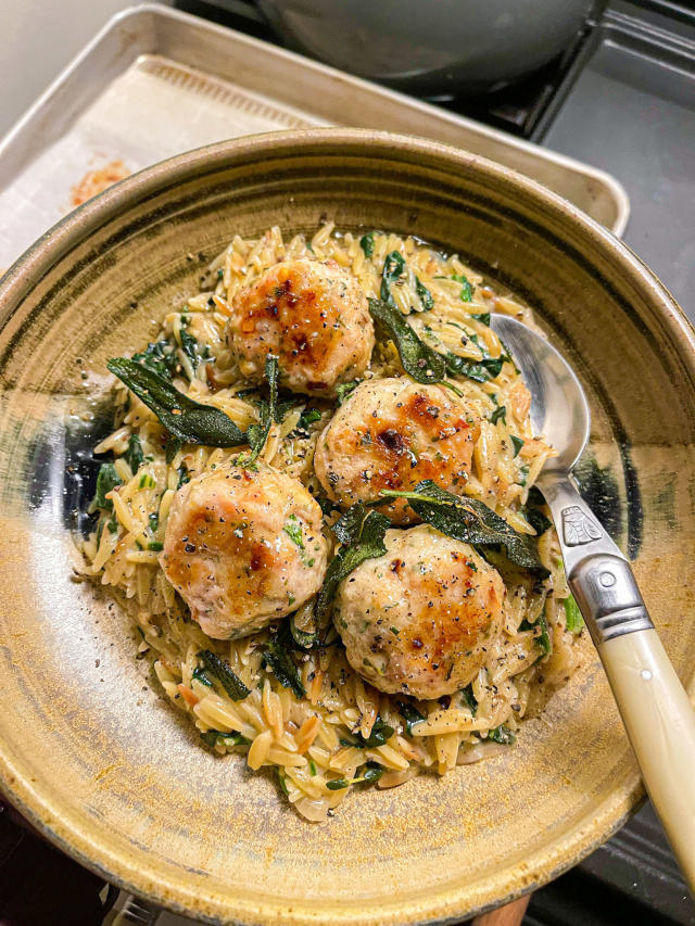 Meatballs on top of creamy orzo and spinach, garnished with sage leaves