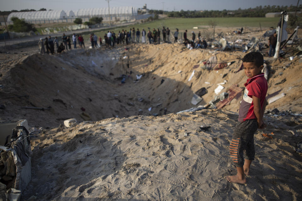 A barefoot Palestinian boy and others look into a crater made in overnight Israeli missile strikes that destroyed a house and killed eight members of the Abu Malhous family, in Deir al-Balah, central Gaza Strip, Thursday, Nov. 14, 2019. (AP Photo/Khalil Hamra)