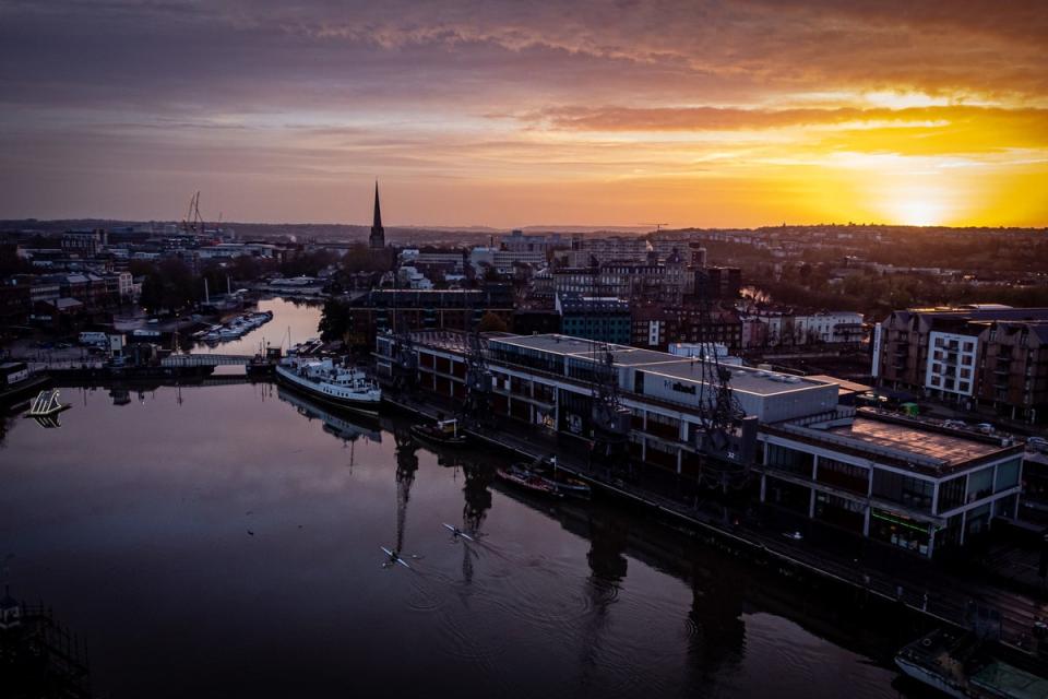 20 November 2022: The sun rises over Bristol Harbourside as rowers cross the basin past the old docks on a cold, but sunny morning across the south west (PA)