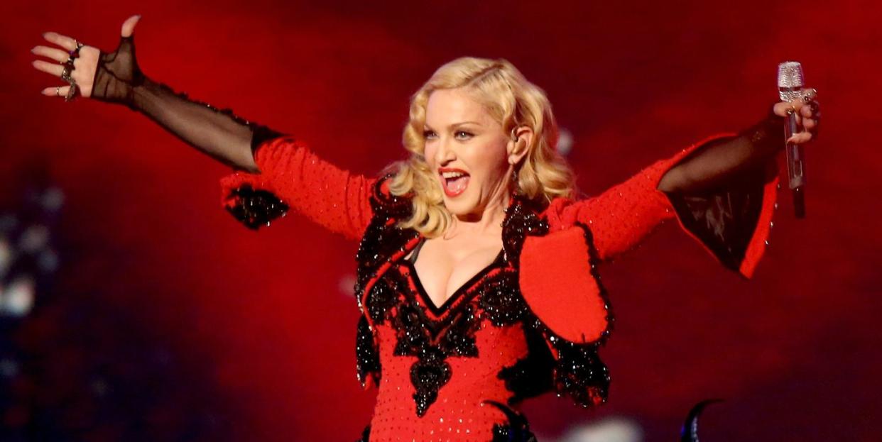 madonna wearing a black and red outfit while extending her arms and holding a microphone on a stage
