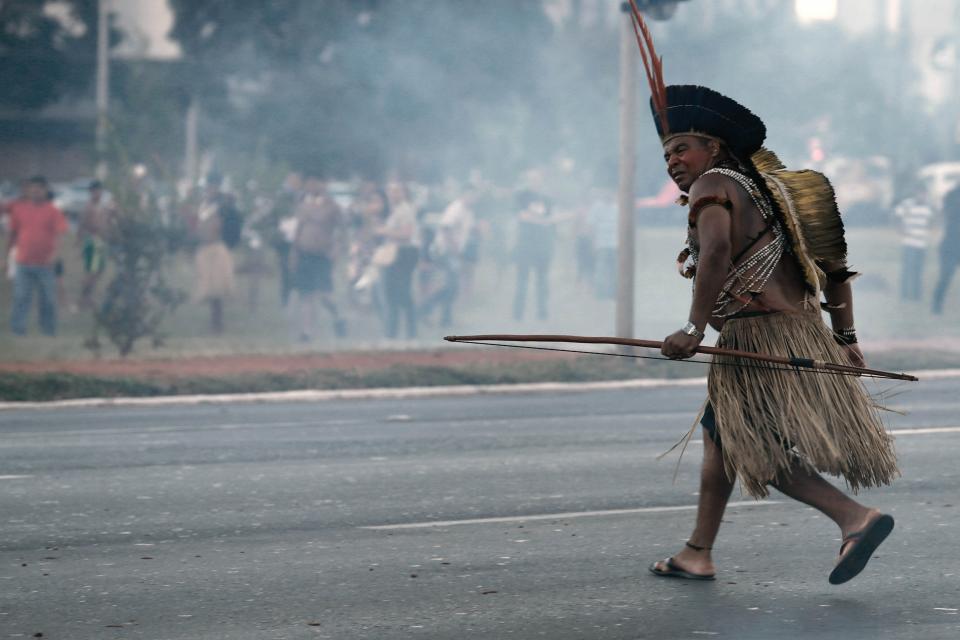 An Indigenous protester in traditional headdress runs with his bow