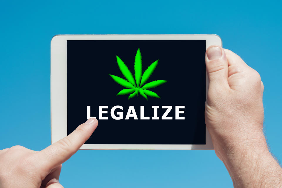 A person touching a tablet screen that shows the word legalize written under a cannabis leaf.