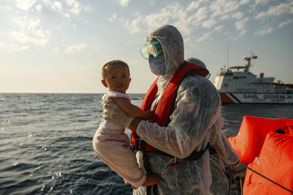 A Turkish coast guard officer, wearing protective gear to help prevent the spread of coronavirus, carries a child off a life raft during a rescue operation in the Aegean Sea, between Turkey and Greece, Saturday, Sept. 12, 2020. Turkey is accusing Greece of large-scale pushbacks at sea — summary deportations without access to asylum procedures, in violation of international law. The Turkish coast guard says it rescued over 300 migrants "pushed back by Greek elements to Turkish waters" this month alone. Greece denies the allegations and accuses Ankara of weaponizing migrants. (AP Photo/Emrah Gurel)