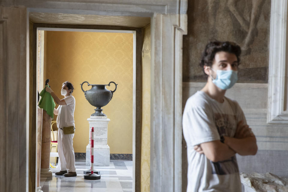 A museum employee cleans a statue, as a visitor wearing face mask to prevent the spread of COVID-19 walks in the Rome's Capitoline Museums, Tuesday, May 19, 2020. In Italy, museums were allowed to reopen this week for the first time since early March, but few were able to receive visitors immediately as management continued working to implement social distancing and hygiene measures, as well as reservation systems to stagger visits to museums in the onetime epicenter of the European pandemic. (AP Photo/Alessandra Tarantino)