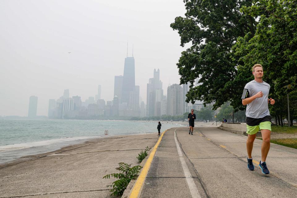 Joggers run along the shoreline of Lake Michigan with heavy smoke from the Canadian wildfires in the background, on June 27, 2023 (AFP via Getty Images)