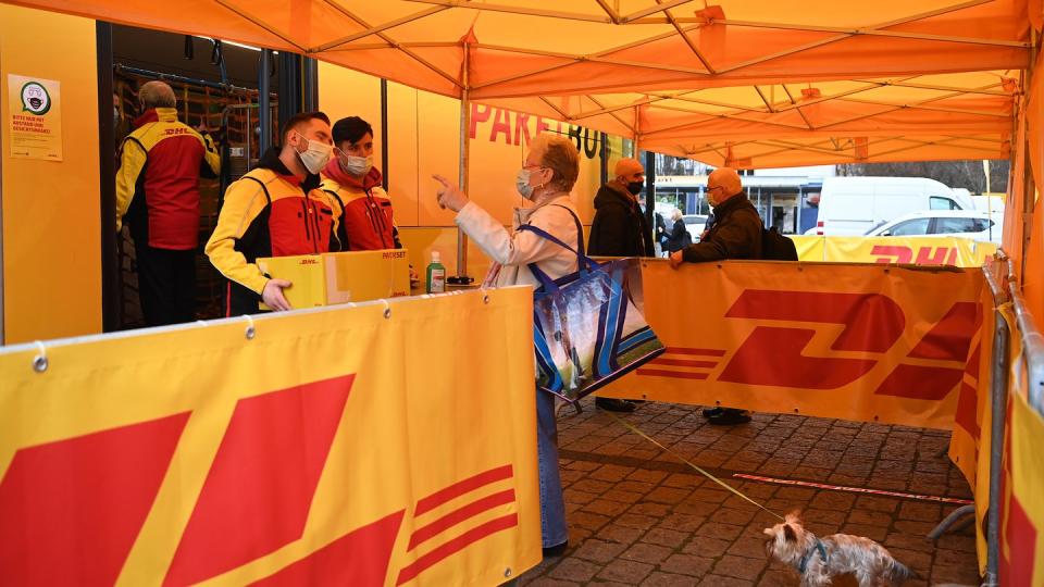 Eine Dame gibt bei Mitarbeitern eines DHL-Paketbusses in Berlin ein Paket ab.