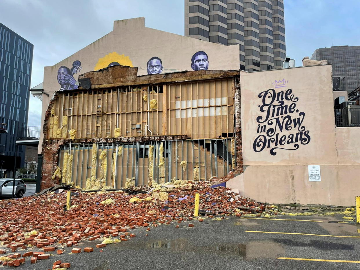 Partially collapsted storefront with bricks scattered over parking lot next to intact wall painted with 