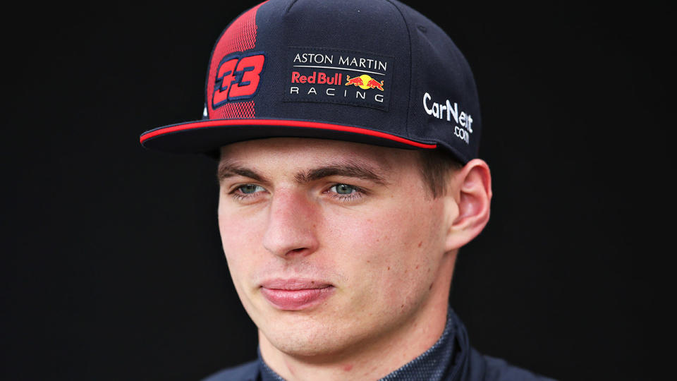 Max Verstappen looks forward and smiles with his Red Bull hat.