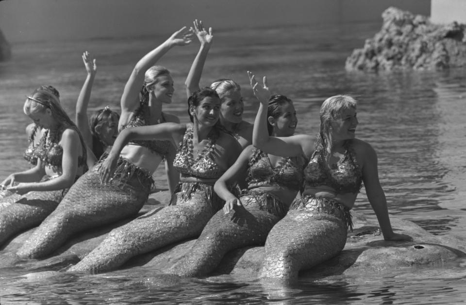 Women dressed as mermaids sit on a rock in the water at Disneyland in the 1950s.