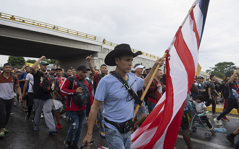 Roberto Marquez carries a U.S. flag and pulls luggage as members of a migrant caravan walk with him as they pass under a bridge