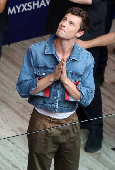 Shawn standing next to a glass railing inside a building and looking with his hands pressed together