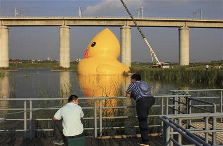 People look on as an inflated Rubber Duck by Dutch conceptual artist Florentijn Hofman is set up next to a high-speed railway viaduct bridge on a lake at the 9th China International Garden Expo in Beijing, September 5, 2013. REUTERS/Stringer