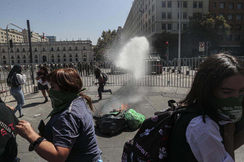 Women run away from a police water cannon as clashes erupt during the International Women's Day Strike in Santiago, Chile, Monday, March 9, 2020. (AP Photo/Esteban Felix)