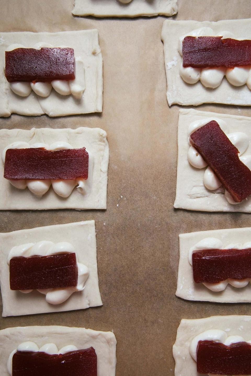 Rows of unbaked pastries with a strip of guava filling on dollops of cream on dough