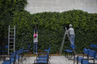 In this Friday May 29, 2020 photo Christina Tsouta, left, cuts leaves as projector operator Pavlos Lepeniotis connects the speakers at the Zephyros open-air cinema that specializes in films from past decades in Athens' central Petralona district. (AP Photo/Petros Giannakouris)