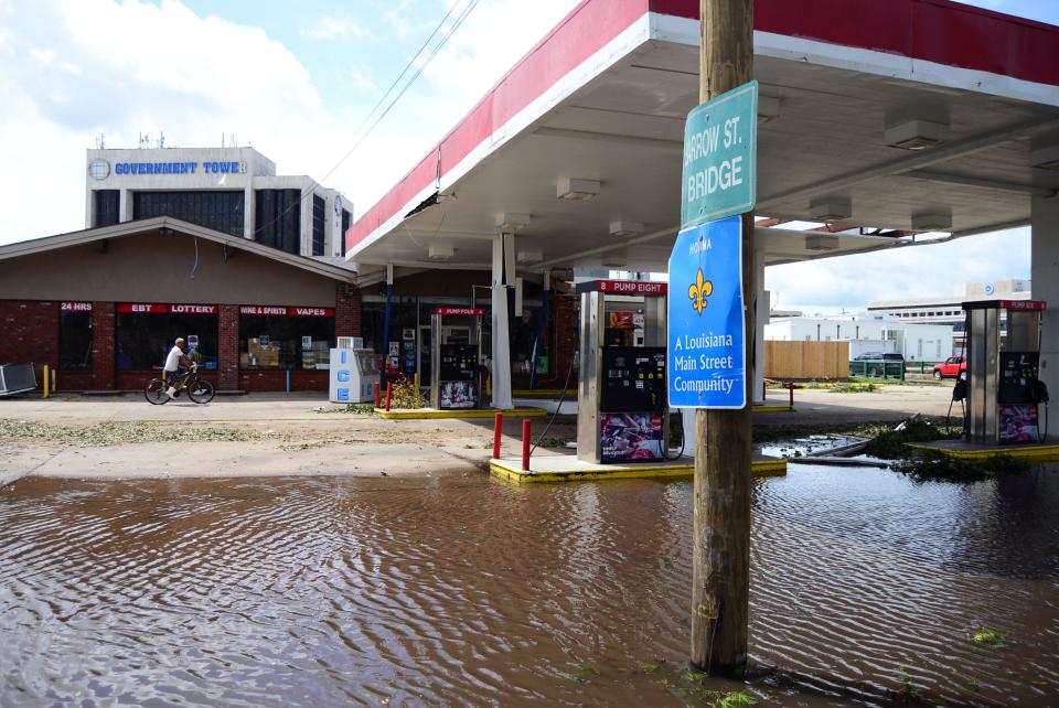 A person is seen riding a bike on Monday, Aug. 30, 2021, past a gas station that has mild flooding in its parking lot in Houma, La.