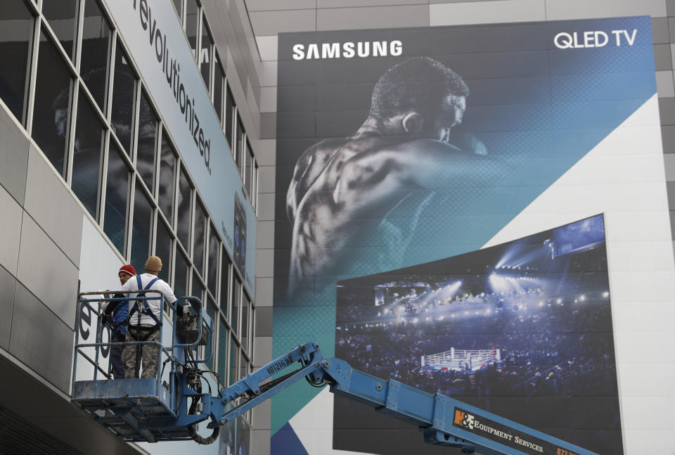 Workers hang up a sign near a Samsung TV banner during setup for CES International, Tuesday, Jan. 3, 2017, in Las Vegas. The show runs from January 5-8. (AP Photo/John Locher)