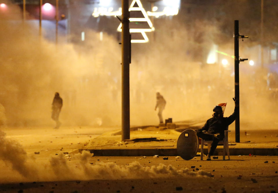 An anti-government protester covered by the smoke of the tear gas, sits in the middle of a street, during a protest against the new government, in downtown Beirut, Lebanon, Wednesday, Jan. 22, 2020. Lebanon's new government, made up of members nominated by the Shiite group Hezbollah and its allies got down to business Wednesday, a day after it was formed. Questions arose immediately about its ability to halt a spiral of economic and political collapse.(AP Photo/Hussein Malla)