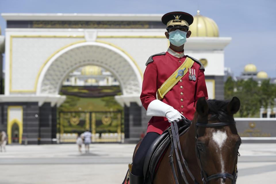 An honor guard member wearing a protective face mask patrols outside National Palace in Kuala Lumpur, Malaysia, Thursday, Feb. 27, 2020. Malaysia's king summoned Mahathir Mohamad to the palace Thursday, fueling talks that he may have majority support to return as the next prime minister after his abrupt resignation and the collapse of his ruling coalition this week. (AP Photo/Vincent Thian)