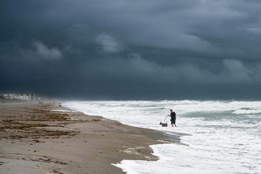 A man walks his dog through the rough surf on Cocoa Beach on September 28, 2022, as the eastern coast of central Florida braces for Hurricane Ian. (Photo by Jim WATSON / AFP) (Photo by JIM WATSON/AFP via Getty Images)
