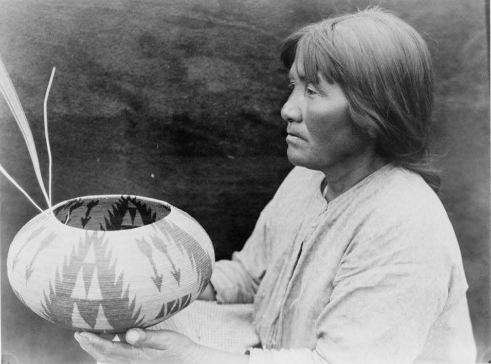 Native American woman, half-length portrait, seated facing left, holding basket.
