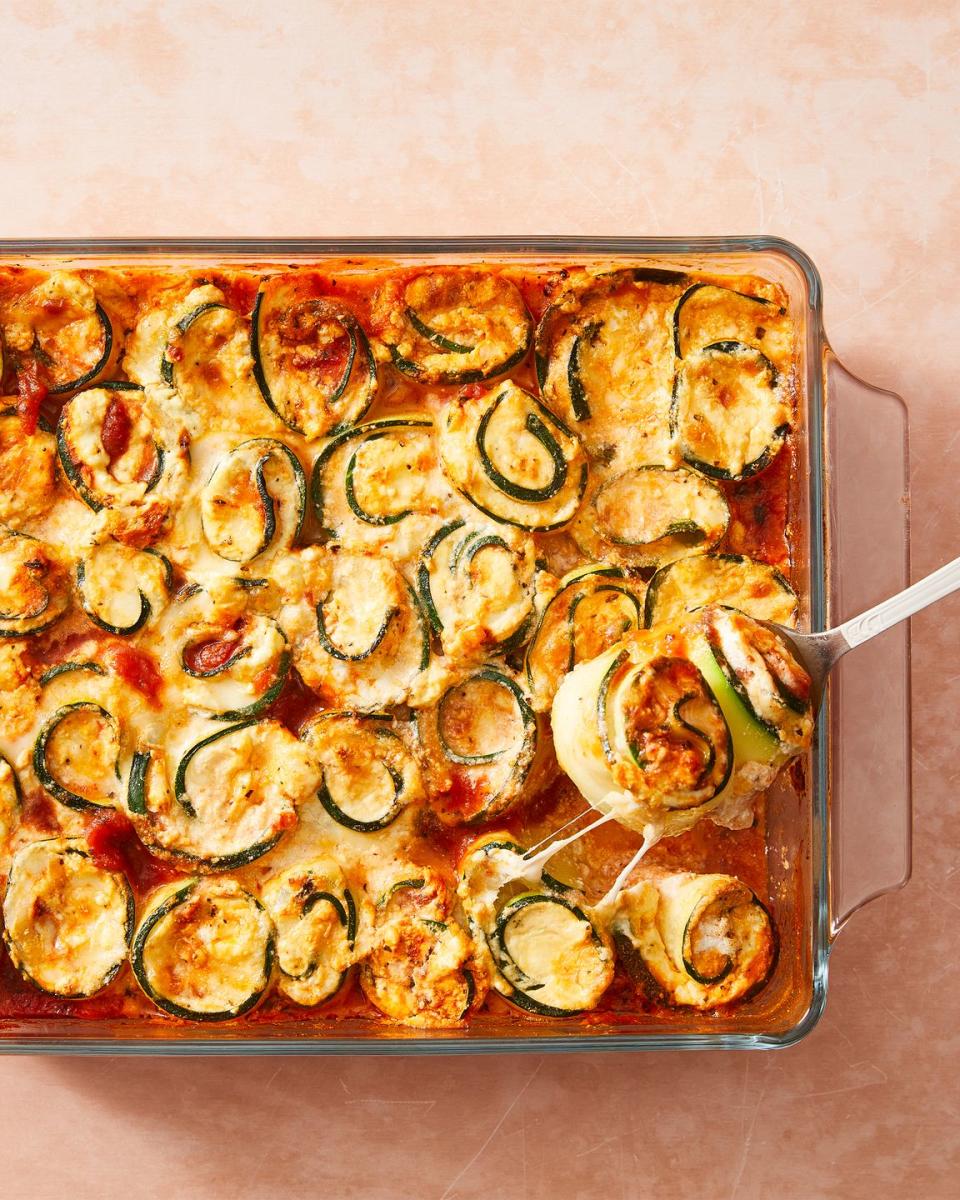 zucchini slices rolled up around cheese with sauce in a casserole dish