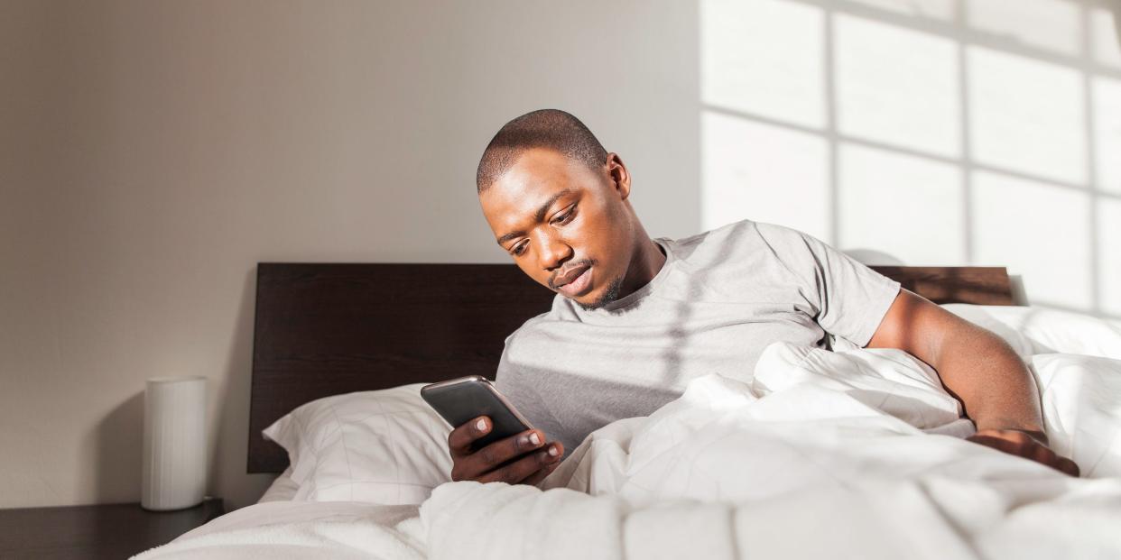 man laying in bed with phone alarm clock waking up