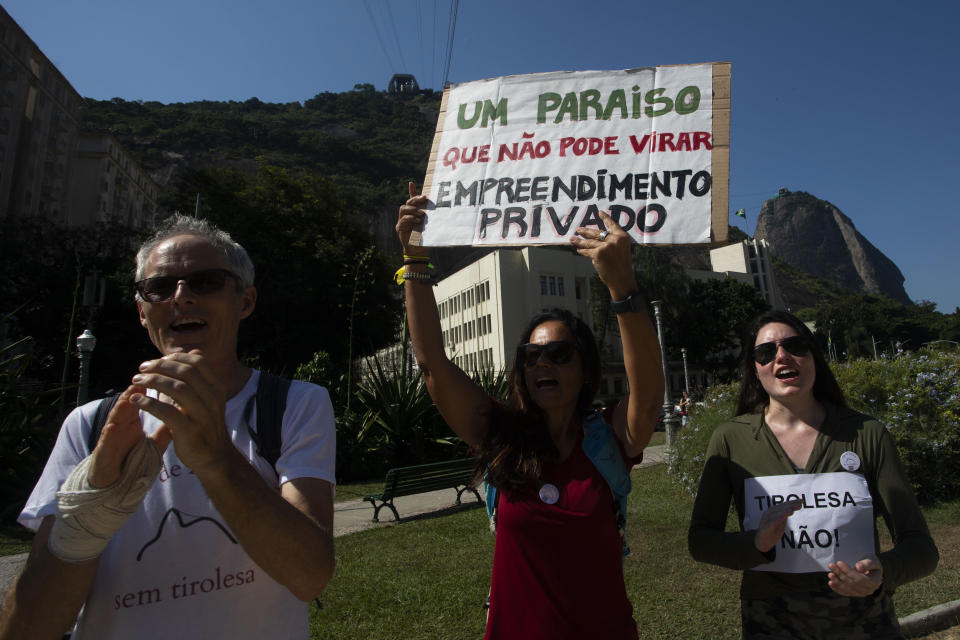 A woman, center, holds a sign that reads in Portuguese "A paradise that cannot become a private enterprise," during a protest against the installation of a zip line on Sugar Loaf Mountain, an iconic of the city and UNESCO World Heritage Site, in Rio de Janeiro, Brazil, Sunday, March 26, 2023. (AP Photo/Bruna Prado)