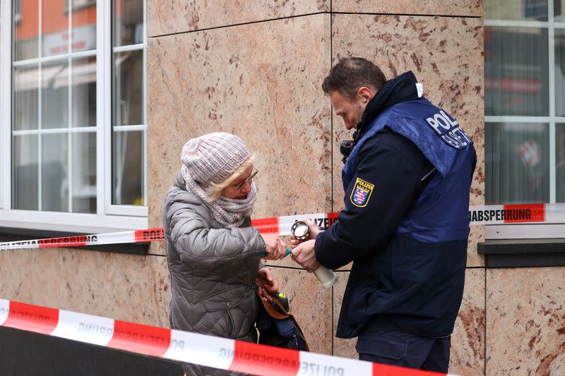 Un oficial de policía ayuda a una mujer a encender una vela para colocarla en un monumento improvisado en el exterior de una de las escenas del crimen, después de un tiroteo en Hanau, cerca de Fráncfort, Alemania