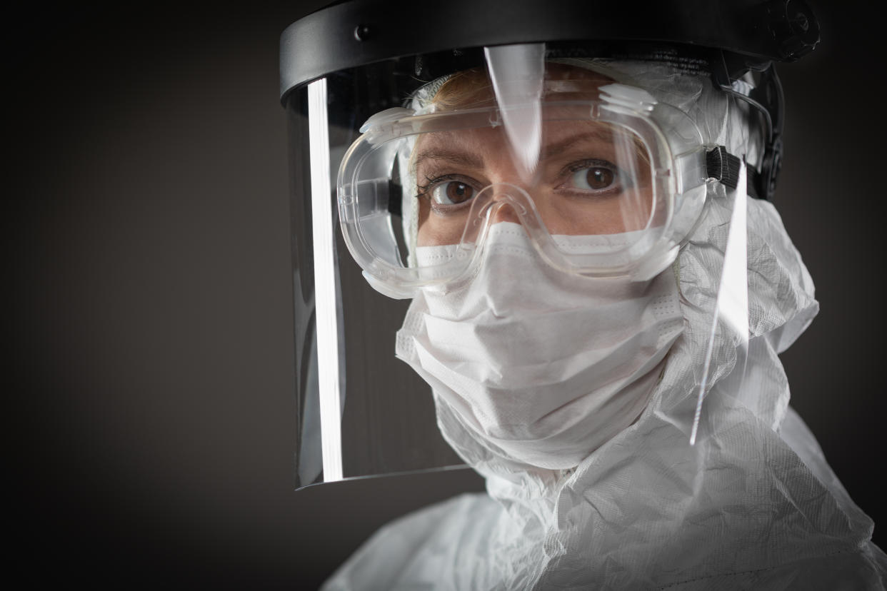 Female Medical Worker Wearing Protective Face Mask and Gear Against Dark Background.