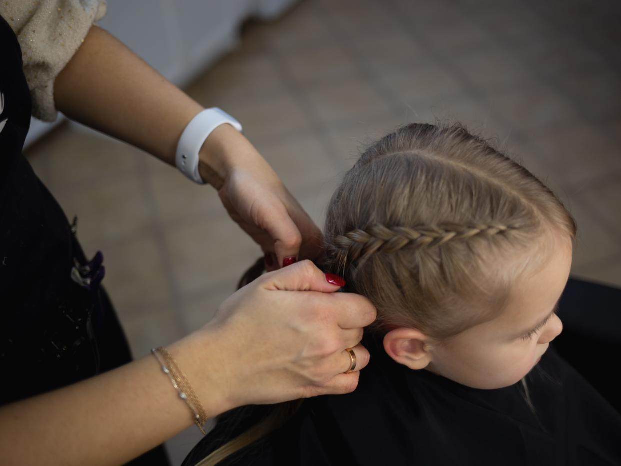 Barber in a hairdressing salon braids pigtails to a little cute girl