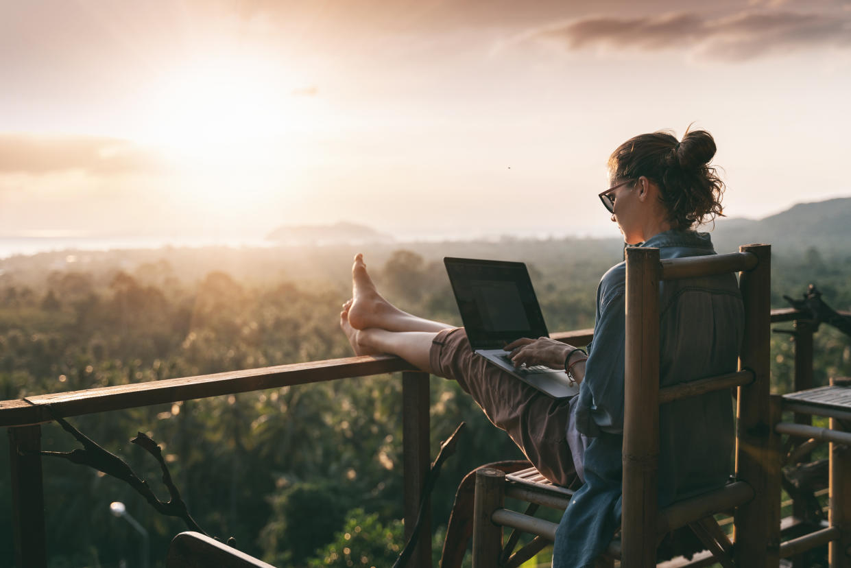 Young business woman working at the computer in cafe on the rock. Young girl downshifter working at a laptop at sunset or sunrise on the top of the mountain to the sea, working day.