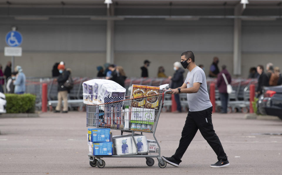 One shopper walks away with a full cart as others queue outside a major supermarket in Leicester, England, Sunday Nov. 1, 2020. The British government announced on Saturday a four-week public lockdown in response to the latest coronavirus surge, and government lawmaker Michael Gove on Sunday acknowledged that the lockdown could be extended. (Joe Giddens/PA via AP)