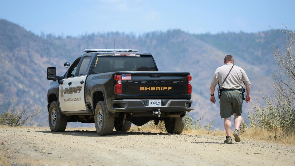 A Mariposa County deputy sheriff stands watch over a remote area northeast of the town of Mariposa, Calif., on Wednesday, Aug. 18, 2021, near the area where a family and their dog were reportedly found dead the day before.