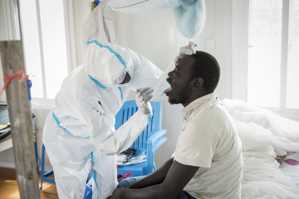 In this photo taken Sunday, June 21, 2020, an infectious disease specialist, left, takes a sample from Dr. Reagan Taban Augustino, right, now a coronavirus patient himself under quarantine, at the Dr John Garang Infectious Diseases Unit in Juba, South Sudan. The United Nations says the country's outbreak is growing rapidly, with nearly 1,900 cases, including more than 50 health workers infected, and at the only laboratory in the country that tests for the virus a team of 16 works up to 16-hour days slogging through a backlog of more than 5,000 tests. (AP Photo/Charles Atiki Lomodong)