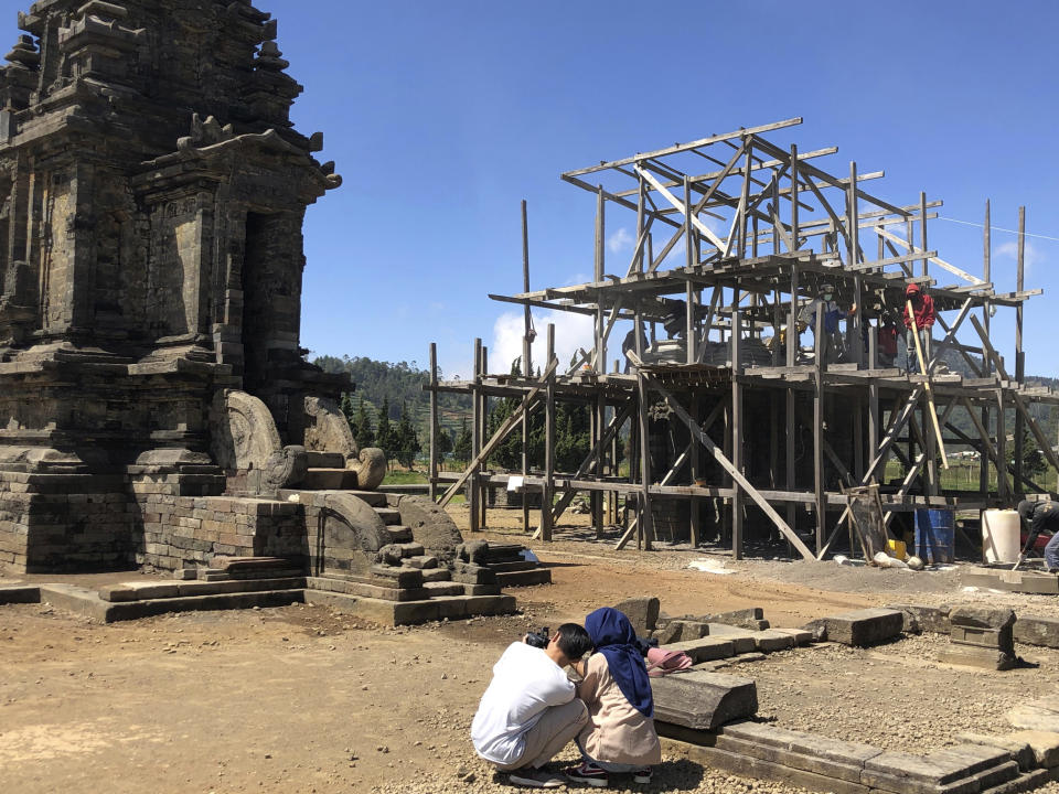 In this July 31, 2019, photo, tourists take photos of temples which is currently under renovation at Arjuna Temple in Dieng, Central Java, Indonesia. The Indonesian city of Yogyakarta and its hinterland are packed with tourist attractions, including Buddhist and Hindu temples of World Heritage. Yet many tourists still bypass the congested city and head to the relaxing beaches of Bali. Recently re-elected President Joko Widodo wants to change this dynamic by pushing ahead with creating "10 new Balis," an ambitious plan to boost tourism and diversify South Asia's largest economy. (AP Photo/Karin Laub)