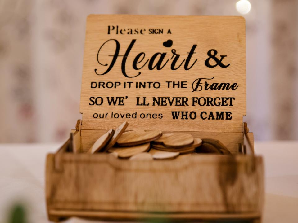 A wooden box with the text "Please sign a heart and drop it into the frame so we'll never forget our loved ones who came"