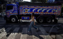 A woman, wearing a face mask, walks in the foreground of a truck in Bangkok, Thailand, Wednesday, May 13, 2020. Thai government continue to ease restrictions related to running business in capital Bangkok that were imposed weeks ago to combat the spread of COVID-19. (AP Photo/Gemunu Amarasinghe)