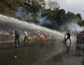 Manifestantes tratan de protegerse de chorros de agua lanzada por vehículos de la policía antimotines en una protesta antigubernamental en Caracas, Venezuela, el miércoles 12 de marzo de 2014. (AP Photo/Fernando Llano)