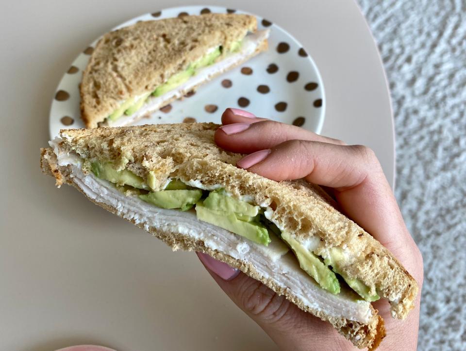 A hand holding a chicken and avocado sandwich.