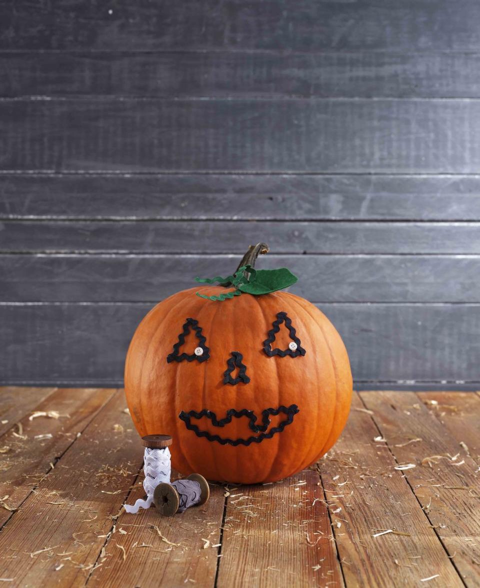 <p>No carving necessary to create this sweet pumpkin face.<strong><br></strong></p><p><strong>Make the pumpkin:</strong> Lightly draw a simple pumpkin face on a pumpkin. Use lengths of black rickrack to cover the drawing, attaching it with hot-glue. Attach small white buttons to the corner of each eye with hot-glue. Cut pumpkin-shaped leaves from green felt and lengths of green rickrack to create tendrils; attach at the base of the pumpkin stem with hot-glue. </p>