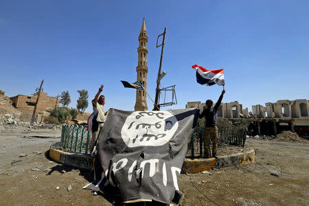 FILE PHOTO: Shi'ite Popular Mobilization Forces (PMF) members hold an Islamic State flag which they pulled down during the war between Iraqi army and Shi'ite Popular Mobilization Forces (PMF) against the Islamic State militants in Tal Afar, Iraq, August 27, 2017. REUTERS/Thaier Al-Sudani/File Photo