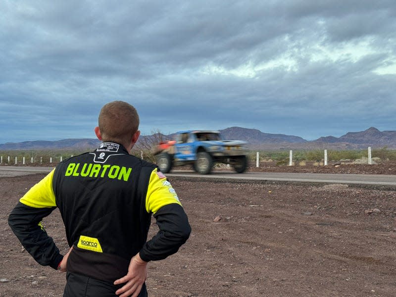 A man standing and watching a Baja race truck drive by