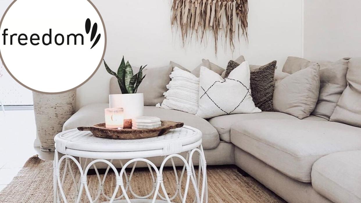 A grey corner sofa in a living room with a white coffee table, and a Freedom Furniture logo on the top left. 