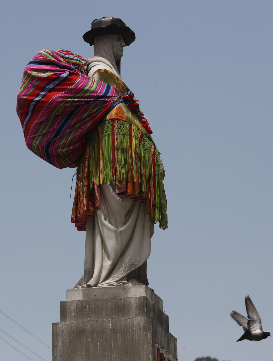 The Queen Elizabeth I monument is covered in an Indigenous "Chola" outfit during a women's protest against Spanish colonization at Isabela Catolica Square in La Paz, Bolivia, Monday, Oct. 12, 2020, as people commemorate Decolonization Day, also known as the Day of the Race. (AP Photo/Juan Karita)