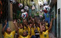 Children throw official 2014 FIFA World Cup soccer balls into the air, as they sit at what is meant to represent a public school classroom, during a protest against the 2014 World Cup, organised by non-governmental organisation (NGO) Rio de Paz (Rio of Peace) at the Jacarezinho slum in Rio de Janeiro May 14, 2014. The protest was held to spread awareness about the need for the standard of Brazil's education system to be raised to that of its preparations for the World Cup, according to the organisation. REUTERS/Sergio Moraes (BRAZIL - Tags: SOCIETY SPORT SOCCER WORLD CUP EDUCATION CIVIL UNREST TPX IMAGES OF THE DAY POVERTY)