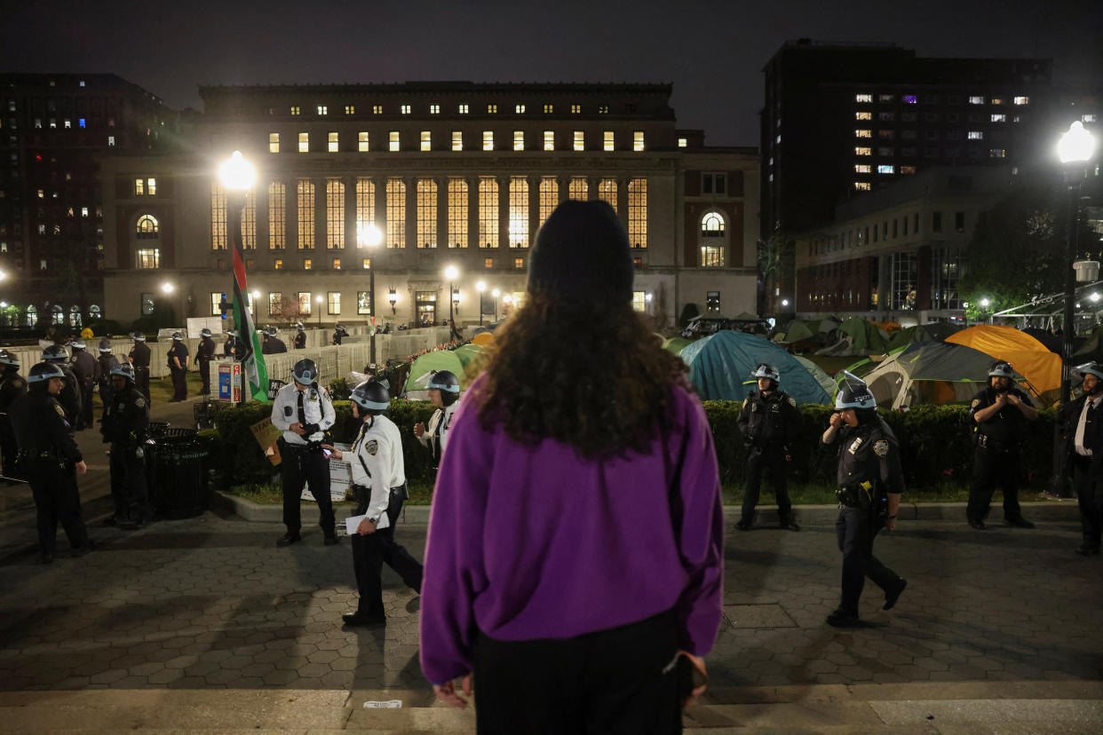 A protester watches police standing guard near an encampment at Columbia University. 