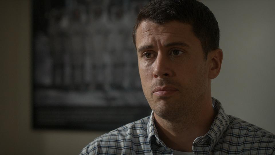 Still from the T.V. show For All Mankind (season 4, episode 1). Close up of a man with short dark hair wearing a blue and white plaid shirt. He looks worried.